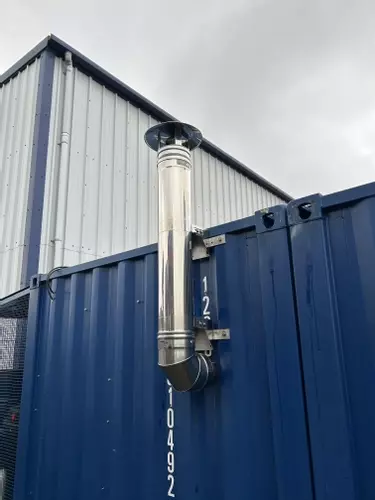 Vertical stainless steel chimney installed on container housing a Nilfisk Truck Booster to safely vent boiler exhaust in Lichfield.